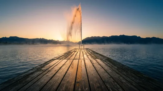 Vue artistique du Jet d'Eau de Genève au lever du soleil, capturé depuis un angle unique avec la jetée déserte