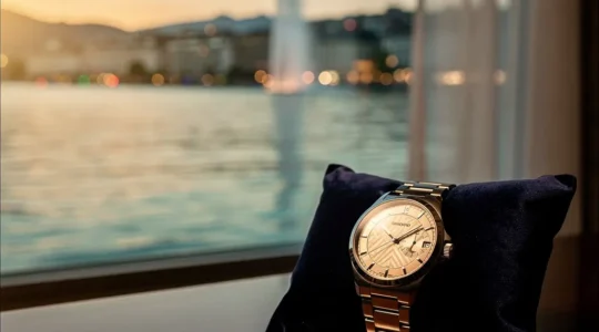Montre de luxe posée sur un coussin de velours avec vue floue sur le lac Léman et le jet d'eau de Genève en arrière-plan