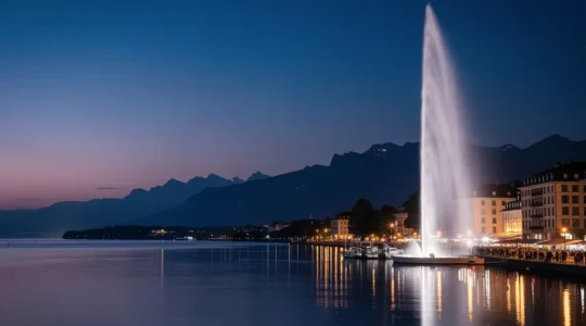 Vue panoramique nocturne de la rade de Genève avec des reflets colorés sur le lac Léman et le Jet d'eau illuminé en arrière-plan